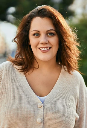 Smiling woman with shoulder-length brown hair in beige sweater outdoors